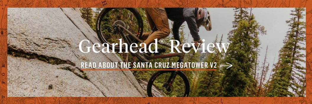 A mountain biker drops down a slabby rock face. The text over lay reads: Gearhead Expert Review. Read about the santa cruz megatower V2.